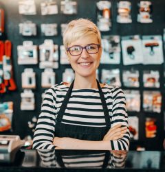 Portrait of beautiful smiling Caucasian female worker with short blonde hair standing in bicycle shop with arms crossed.